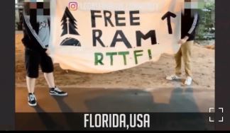 Two people stand outdoors on sandy ground holding a cream-colored banner, their faces obscured. The banner reads "FREE RAM" in large black stencil letters, with a black pine tree emblem on the left side, an upward-pointing arrow on the right, and "RTTF!" in green letters along the bottom edge. An Instagram logo watermark appears in the upper left corner. Text at the bottom of the frame reads "FLORIDA,USA" in white capitals on a dark bar. Both people wear dark tops and shorts or pants with sneakers.