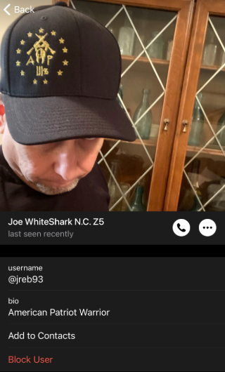 A screenshot of a messaging app contact profile. The profile photo shows a person in a black baseball cap with gold embroidery featuring star patterns, letters, and Chinese characters. Display name reads "Joe WhiteShark N.C. Z5," username is "@jreb93," and bio reads "American Patriot Warrior." Options include "Add to Contacts" and "Block User."