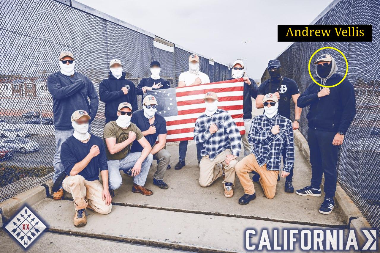 A photo of a dozen masked patriot front members posing with their fists over their chests. Andrew Vellis is circled on the far right.
